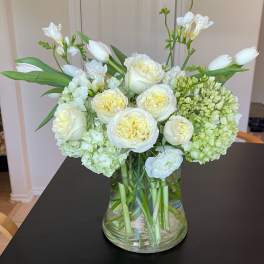 White roses and tulips arranged in a clear glass vase