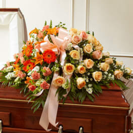 Casket spray with peach roses, orange gerbera daisies, and a pink ribbon