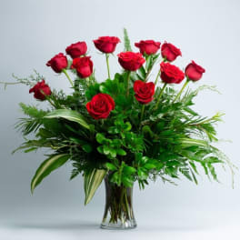 Red roses arranged in a clear glass vase with lush greenery