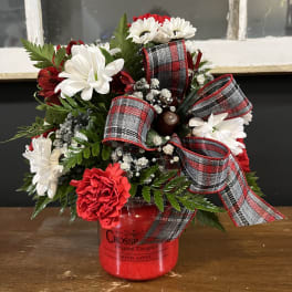 Red and white flower arrangement in a red jar with plaid ribbon