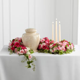 Pink rose and carnation floral centerpiece around a beige urn with three candles