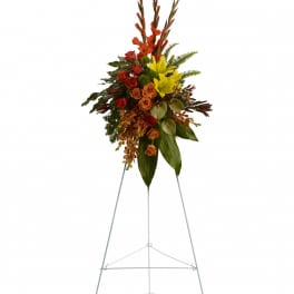 Tall floral standing spray with red, orange, and yellow blooms on a metal easel