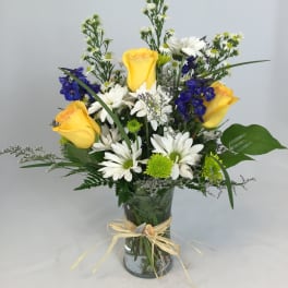 Yellow roses and white daisies in a glass vase with blue flowers