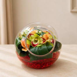 Round glass vase with orange and green flowers and red filler