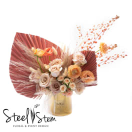 Bouquet of blush and peach roses in a gold vase with fan-shaped dried accents