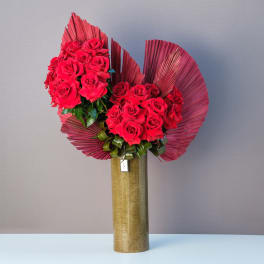 Two red rose bouquets in a tall gold vase with fan-shaped red leaves
