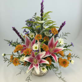 Basket arrangement with pink lilies, orange daisies, and purple accents