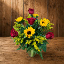 Red roses and yellow sunflowers in a clear glass vase