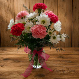 Pink and white carnations with daisies in a glass vase tied with a pink ribbon
