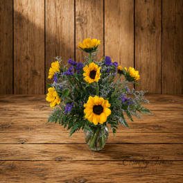 Sunflower bouquet in a clear glass vase with purple filler flowers