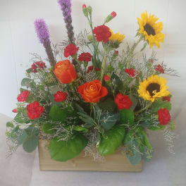 Mixed bouquet with orange roses, red carnations, and yellow sunflowers in a wooden box