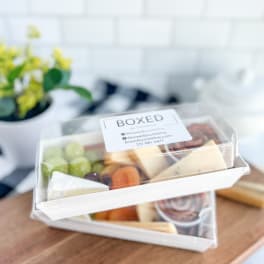Two stacked clear-lidded snack boxes with fruit and cheese