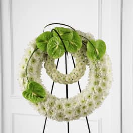 White floral wreath on a black stand with bright green anthurium accents