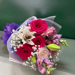 Bouquet of pink roses, white lily, and purple flowers wrapped in clear paper