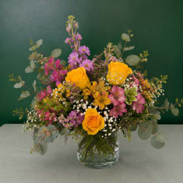 Mixed bouquet of yellow roses and pink flowers in a glass vase