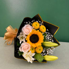 Bouquet of sunflowers, pale pink roses, and white lilies wrapped in black paper