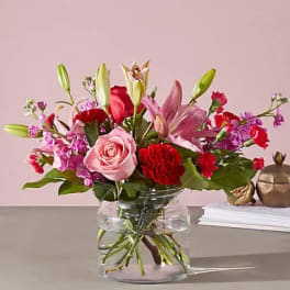 Mixed pink and red flowers arranged in a clear glass vase