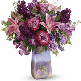 Pink lilies and roses arranged in a tall iridescent vase