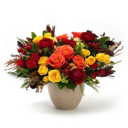 Low arrangement of red, orange, and yellow roses with ranunculus in a beige ceramic vase.