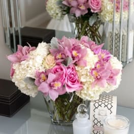 Pink orchids and roses arranged with white hydrangeas in a glass vase