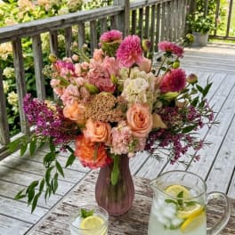 Pink and peach bouquet in a mauve vase on an outdoor table