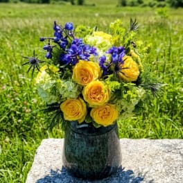 Yellow and blue flower bouquet in a dark vase outdoors
