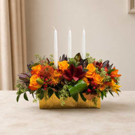 Orange and red floral centerpiece with three white candles in a gold container