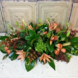 Low floral centerpiece with peach blooms and green foliage