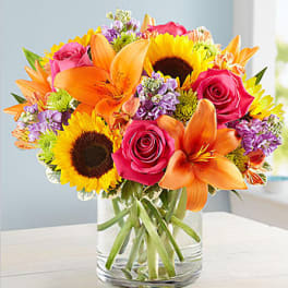 Bright bouquet of sunflowers, orange lilies, and pink roses in a glass vase