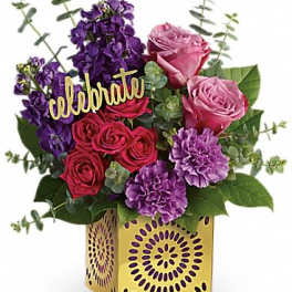 Bright arrangement of pink and red roses with purple flowers in a gold cube vase with a celebrate sign.