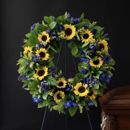 Sunflower and blue flower funeral wreath on a stand