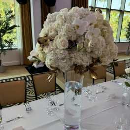 Large white floral centerpiece in a tall glass vase on a set dining table