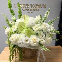 White floral arrangement in a wicker basket with green accents