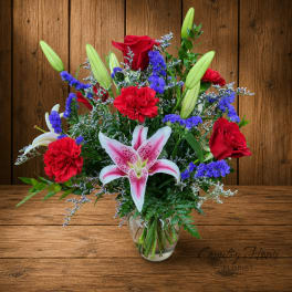 Bouquet of red roses, red carnations, and pink lilies in a clear glass vase