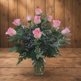 Pink roses arranged in a clear glass vase with mixed greenery