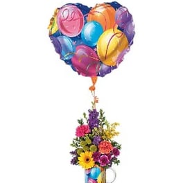 Heart-shaped balloon above a colorful flower arrangement in a mug