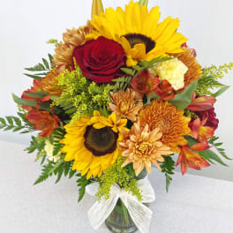 Mixed bouquet with sunflowers, red roses, and orange mums in a glass vase
