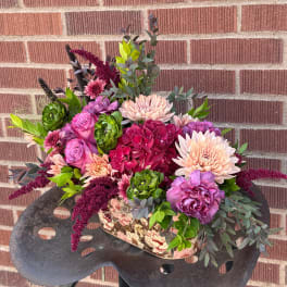 Mixed bouquet in a floral-patterned container with pink, peach, and purple blooms