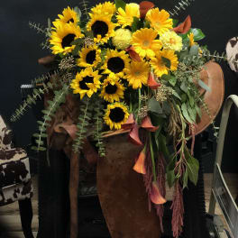 Large bouquet of yellow sunflowers and orange calla lilies in a rustic container