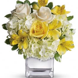 Yellow and white flower arrangement in a clear square vase
