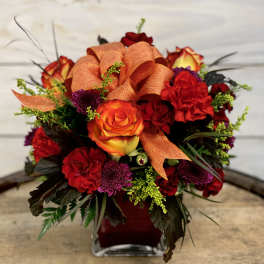 Orange and red rose bouquet in a square glass vase