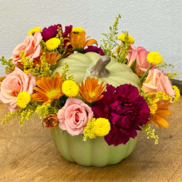 Floral arrangement in a pale green pumpkin-shaped container with pink, orange, and yellow blooms
