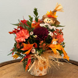 Fall floral arrangement with a scarecrow topper in a decorated vase