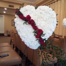 Heart-shaped white floral arrangement with red roses on an easel