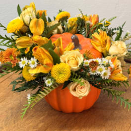 Fall floral arrangement in a pumpkin container with yellow and orange blooms