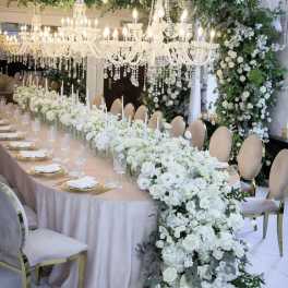 White floral wedding table with chandeliers and a long centerpiece