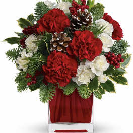 Red and white floral arrangement in a red glass vase with pinecones