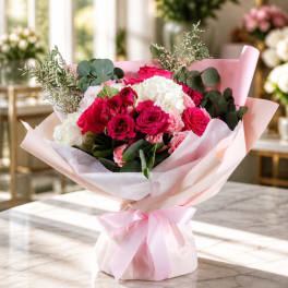 Pink and white rose bouquet wrapped in pale pink paper with a ribbon