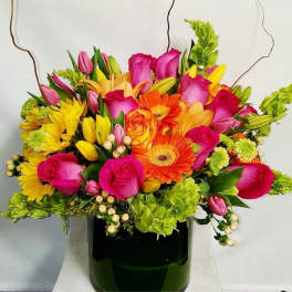 Bright mixed bouquet with pink roses, orange gerberas and yellow blooms in a dark green vase