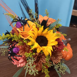 Autumn floral arrangement with sunflowers, roses, and Halloween spider decorations in a pumpkin container